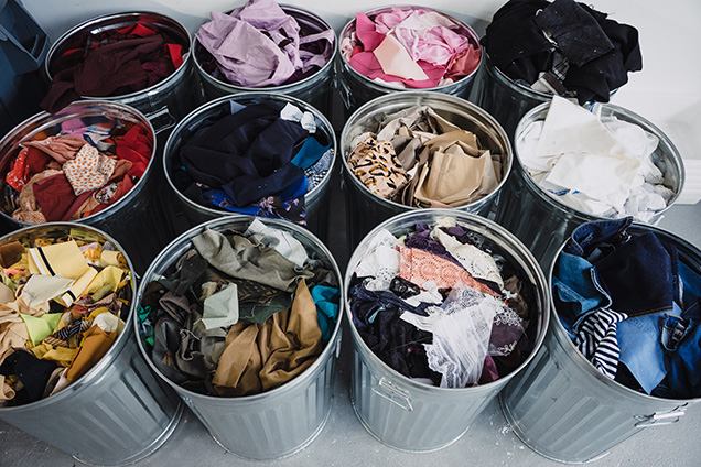 Several buckets of clothes in trashcans.